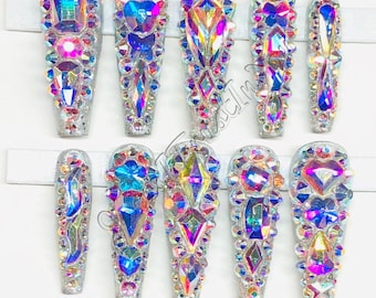 Puede incluir: Conjunto de diez uñas postizas largas, plateadas, con diamantes de imitación iridiscentes de diferentes formas y tamaños.