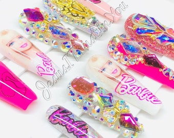 May include: Set of pink and white press-on nails with rhinestones and glitter. The nails feature the word "Barbie" written on them.