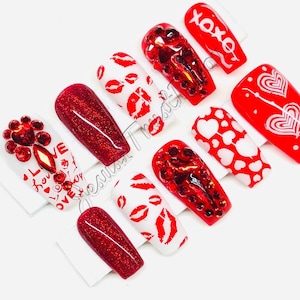 May include: Set of ten red and white Valentine's Day themed press-on nails. The nails feature different designs including hearts, lips, and the words "I love you" and "xoxo".