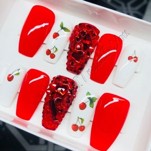 May include: Set of ten red and white press-on nails with cherry designs and red rhinestone accents.
