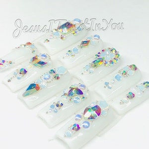 May include: White press-on nails with iridescent rhinestones and crystals arranged in a decorative pattern. The nails are decorated with the text "Jesus I Trust In You".