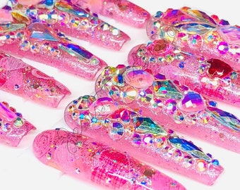 May include: Pink long false nails with glitter and rhinestones.