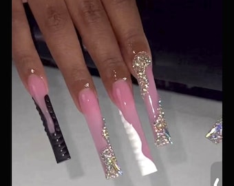 May include: Long, pink, and white acrylic nails with rhinestones and a black accent nail.