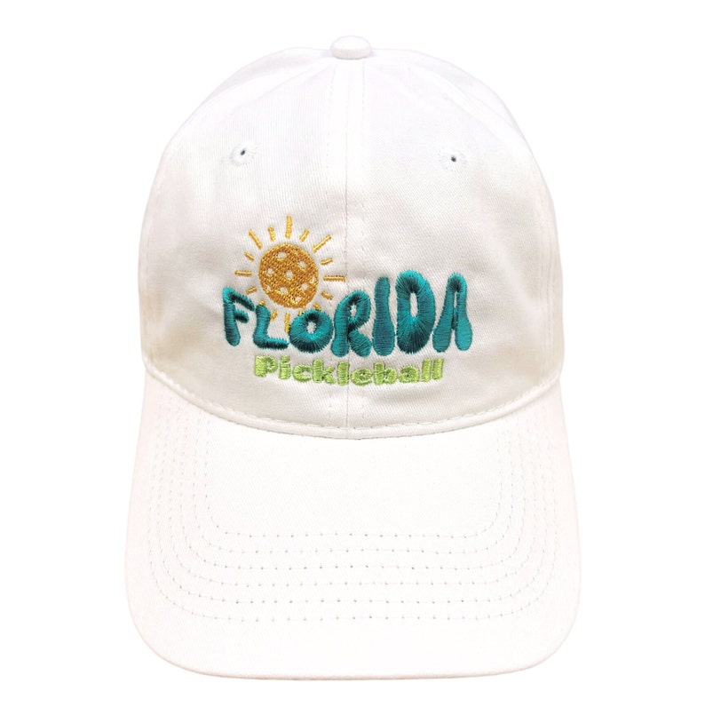 Pode incluir: Bon&eacute; de beisebol branco com um design bordado que apresenta um sol, uma bola de pickleball e o texto "Florida Pickleball".