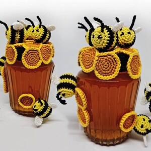 Puede incluir: Varios frascos de vidrio llenos de un líquido dorado, adornados con abejas y diseños de panal de abeja de ganchillo amarillo y negro. Los frascos están decorados con abejas y patrones de panal de ganchillo, creando una estética artesanal y caprichosa.