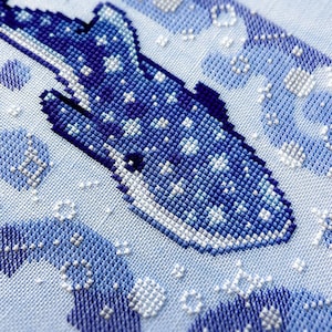 May include: A cross-stitch design of a whale shark in shades of blue and white. The whale shark is the focal point, with a detailed pattern of stitches. The background features abstract shapes and bubbles, all in a light blue hue.