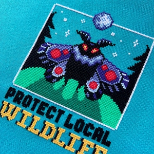 May include: A cross-stitch design featuring a black moth with red and purple accents, set against a teal background. The design includes the text "PROTECT LOCAL WILDLIFE" in yellow and black.