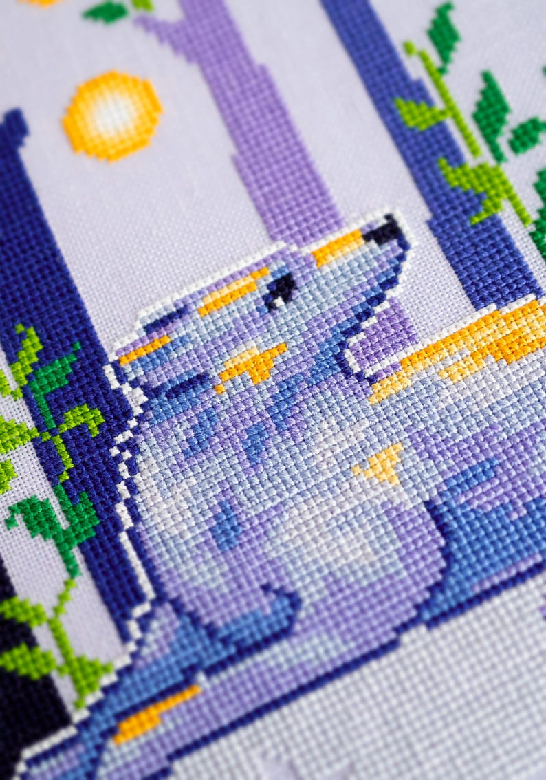 May include: A cross-stitch design featuring a wolf howling at the moon. The artwork uses shades of blue, purple, and yellow. The wolf is the focal point, with a detailed depiction of its fur and expression. The background includes stylized trees and foliage.
