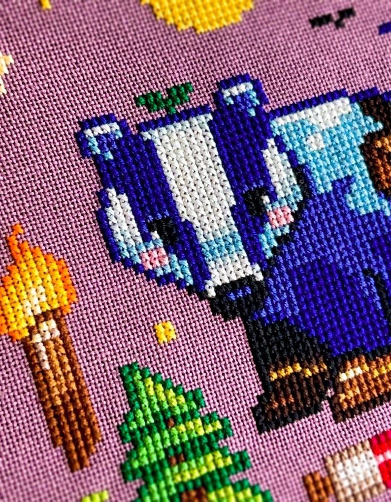 Puede incluir: Arte de punto de cruz con un personaje pixelado azul y blanco con botas marrones, un &aacute;rbol verde y una antorcha. El fondo es una tela de color p&uacute;rpura claro. Otros elementos pixelados incluyen un sol amarillo y un objeto a rayas rojas y blancas.