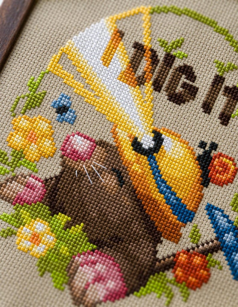 Peut inclure: Une broderie au point de croix sur tissu beige repr&eacute;sentant une taupe brune portant un casque de chantier jaune et tenant une pelle. Le texte "DIG IT" est brod&eacute; en brun au-dessus de la taupe, entour&eacute; de fleurs color&eacute;es, de feuilles vertes et d'un petit papillon bleu.