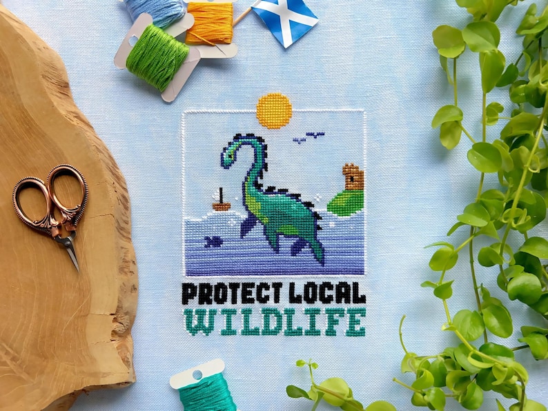 May include: Cross-stitch pattern featuring a green and blue sea monster with the text "Protect Local Wildlife" in black.