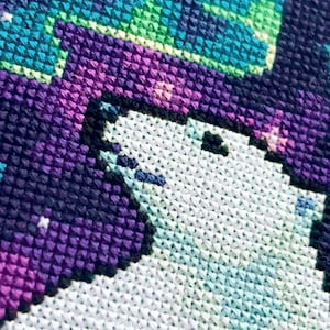 May include: Close-up of a cross-stitch pattern featuring a white polar bear with a purple and black background. The background has a pixelated design with a gradient of purple, black, and blue.