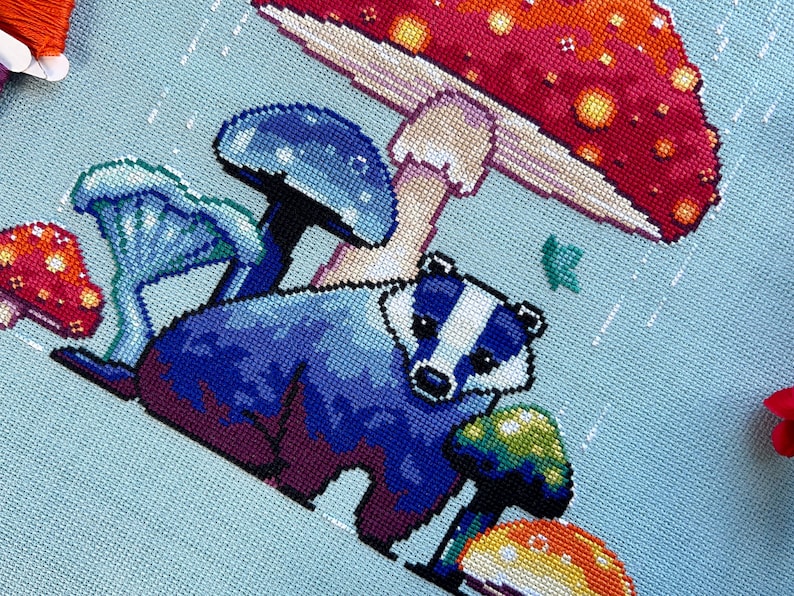 May include: A blue badger standing under a red and yellow mushroom with white spots. There are other blue mushrooms in the background.