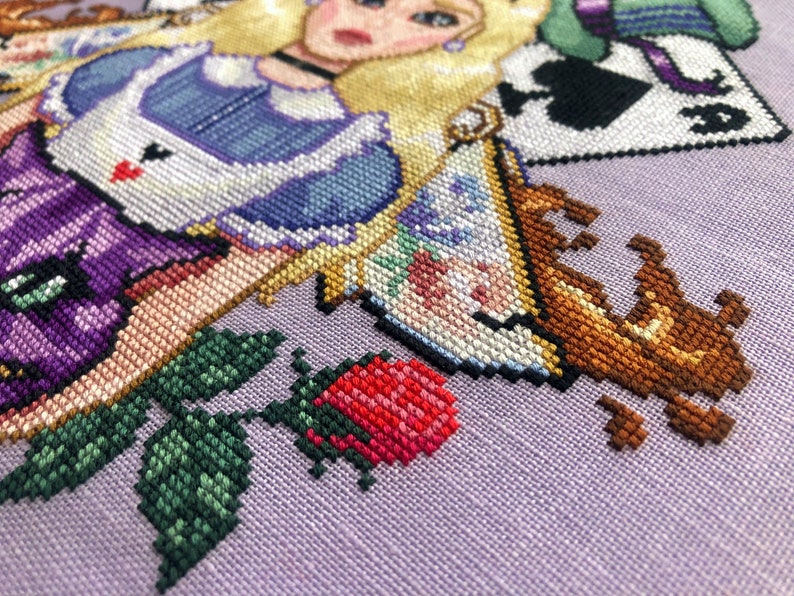 Closeup of righthand bottom side of Alice in Wonderland cross stitch pattern. One of the roses and teacups are particularly visible here. The teacup is a traditional English teacup, which brown tea is spilling out of. The rose is red and pink.