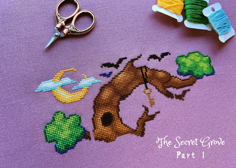 May include: Cross stitch pattern of a brown tree with a key hanging from a branch, a crescent moon, and three green shamrocks. The text "The Secret Grove Part 1" is stitched below the tree.
