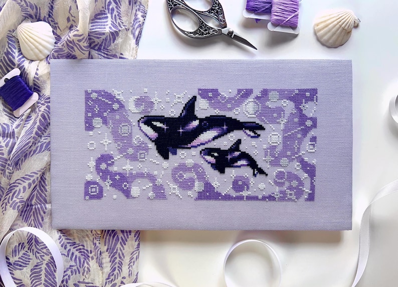May include: A purple cross-stitch embroidery of two orcas swimming in a sea of abstract shapes and patterns.