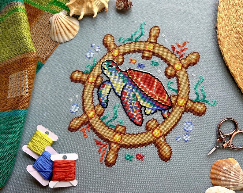 May include: A colorful cross-stitch pattern of a sea turtle swimming in a circle with a wooden ship's wheel. The turtle is red, green, blue, and yellow. The wheel is brown with yellow accents.