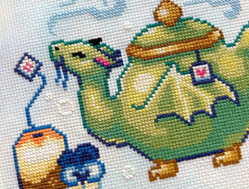 May include: A green teapot with a brown lid and a dragon design. The teapot is sitting on a white background with a blue and pink flower.