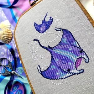 Slight closeup and angled view of ocean rays cross stitch pattern. Cross stitch pattern is of small to medium size. White bubbles are minimalist. Colors are vibrant and beautiful. Rays are soaring through the water.