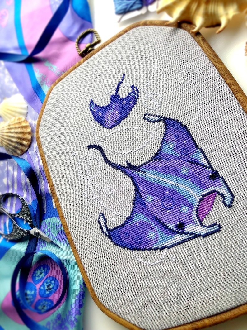 Slight closeup and angled view of ocean rays cross stitch pattern. Cross stitch pattern is of small to medium size. White bubbles are minimalist. Colors are vibrant and beautiful. Rays are soaring through the water.