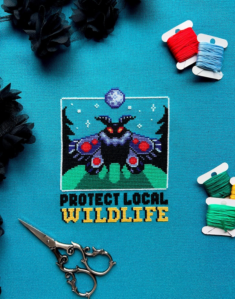 May include: A cross-stitch design on turquoise fabric featuring a black moth with red and purple accents, set against a green landscape and a starry sky. The text "PROTECT LOCAL WILDLIFE" is stitched below. Spools of thread and scissors are also visible.