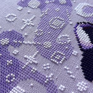 May include: Close-up of a purple and white cross-stitch pattern. The pattern is made up of small squares, and the colors are arranged in a geometric design.