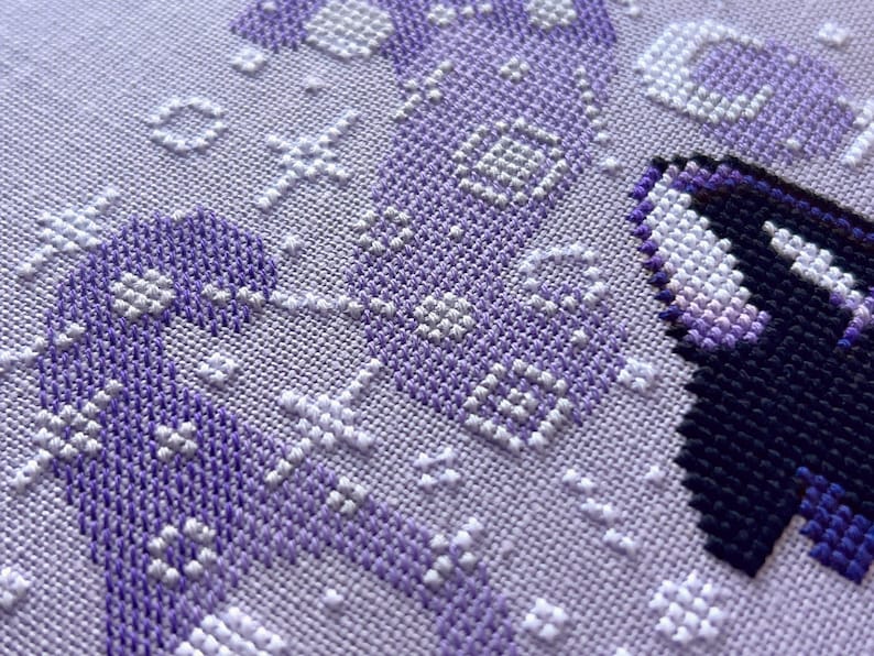 May include: Close-up of a purple and white cross-stitch pattern. The pattern is made up of small squares, and the colors are arranged in a geometric design.
