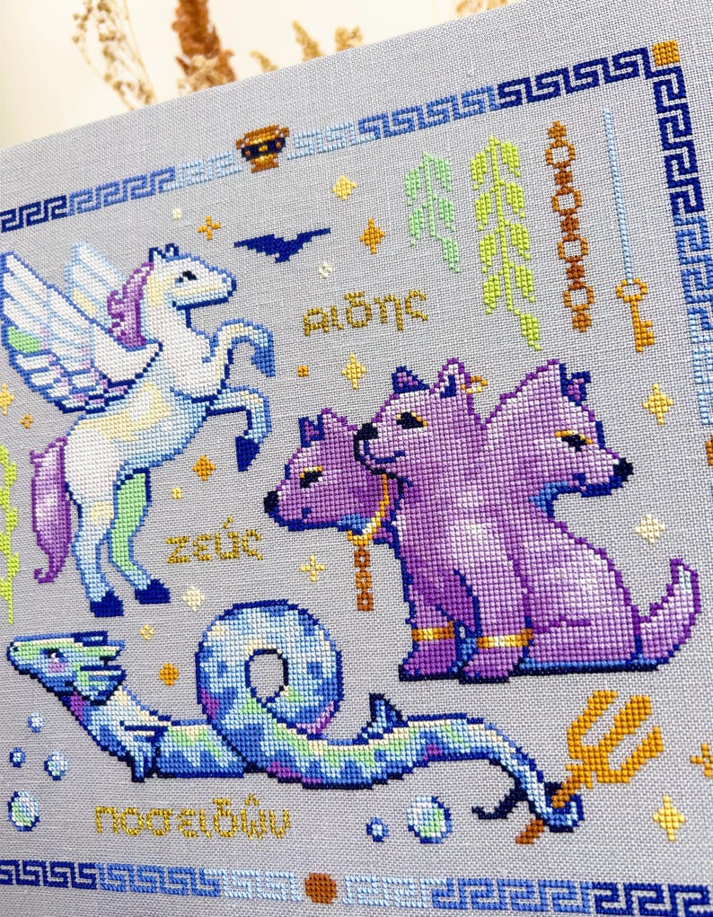 May include: Cross-stitch art featuring mythological creatures on a light gray background. A winged horse, a three-headed dog, and a sea serpent are depicted in shades of blue, purple, and green. The Greek words "Zeus", "Poseidon", and "Alone" are stitched in gold.