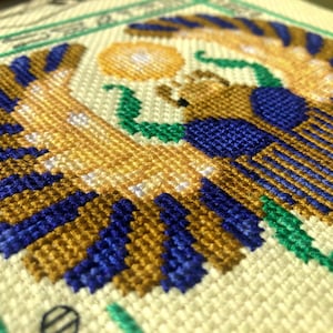 Closeup of Egyptian scarab cross stitch pattern. Angled view of the bottom left. Stitches are tidy. Colors are bright and beautiful.