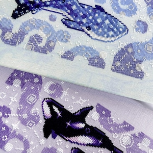May include: Cross-stitch art featuring a whale shark in shades of blue and white, swimming amidst stylized waves. The second piece showcases orcas in black and purple, with a smaller orca alongside. Both pieces have a celestial theme.