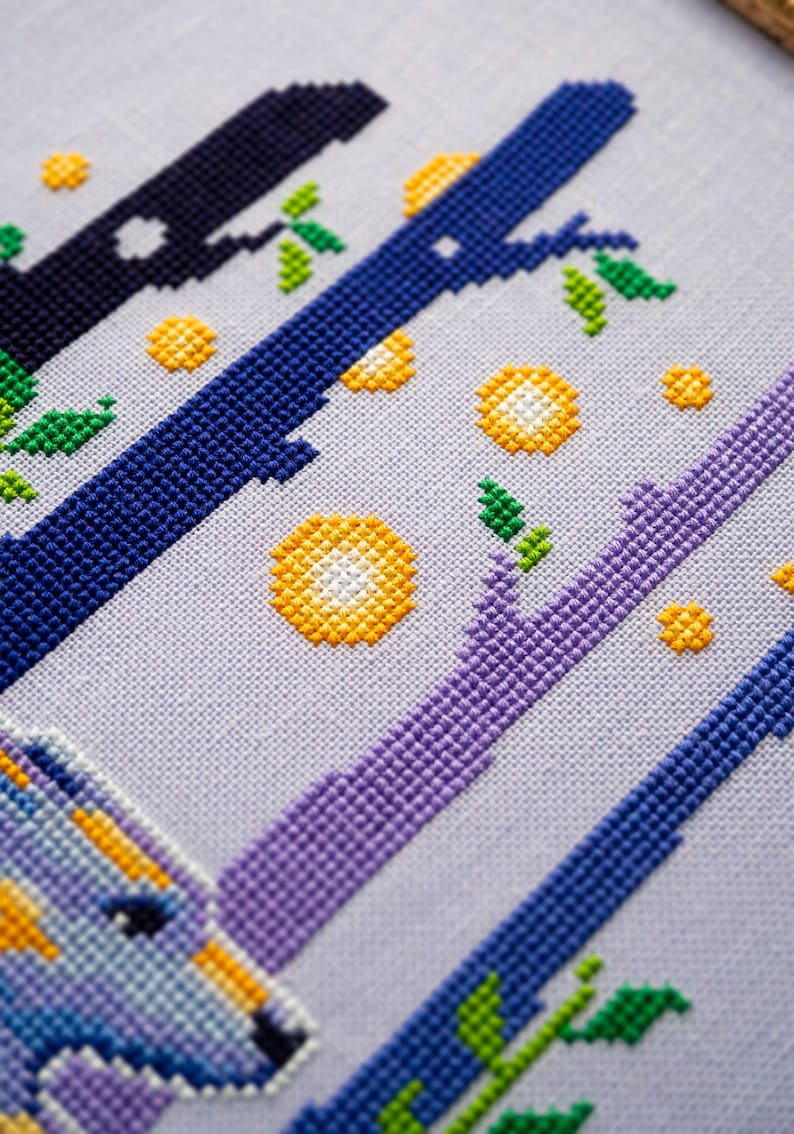 May include: Cross-stitch embroidery featuring a stylized design of branches and circular shapes in shades of blue, purple, yellow, and green on a light gray fabric. The design includes a partial image of a unicorn.