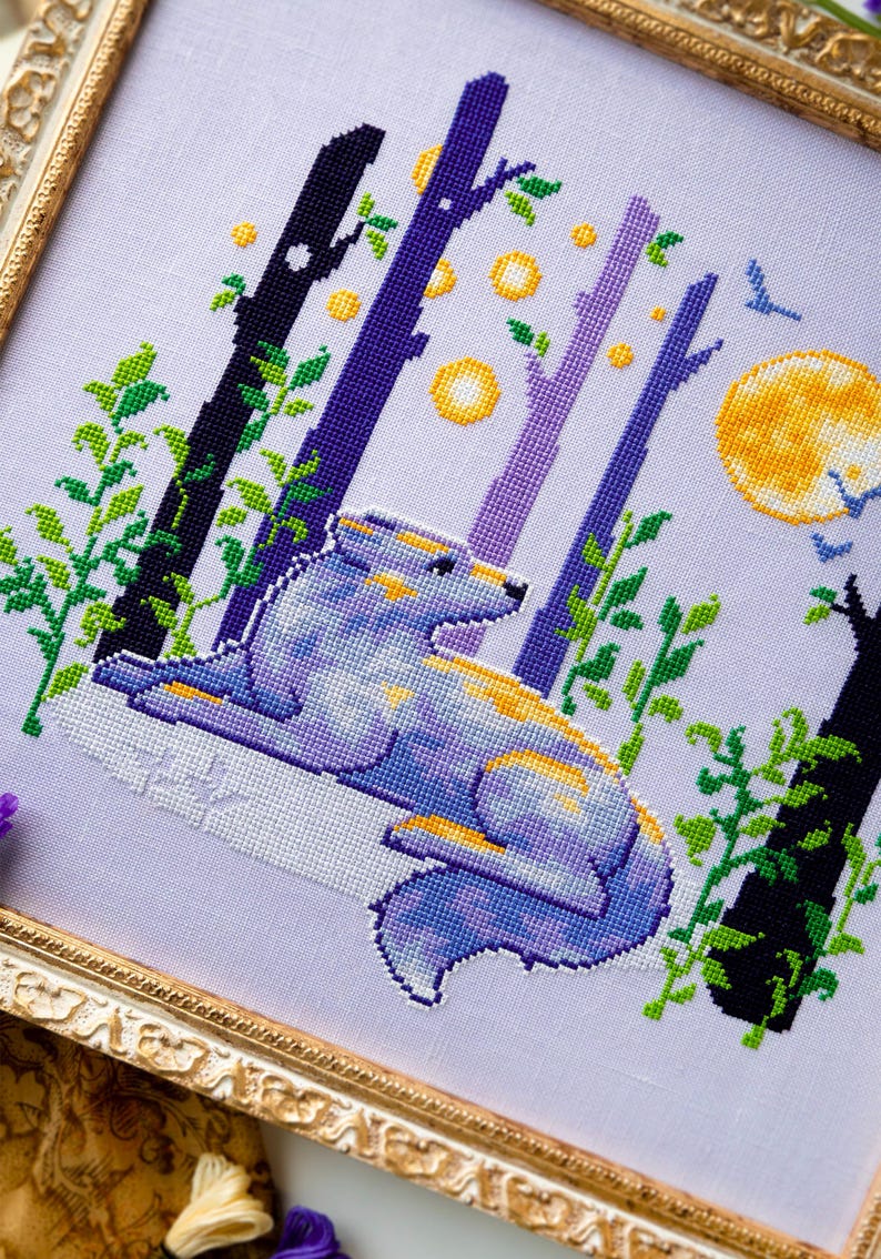 May include: Cross-stitch art of a wolf in a forest scene. The wolf is blue, purple, and yellow, lying down with a full yellow moon in the background. The trees are black, purple, and white with green leaves. The artwork is framed in a gold frame.
