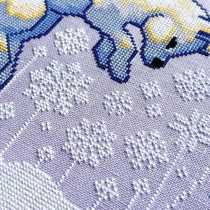 May include: A close-up of a cross-stitch pattern featuring a blue and yellow animal with white snowflakes on a purple background.