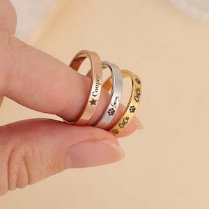 May include: Three personalised rings with engraved names and paw prints. The rings are gold, silver and rose gold.