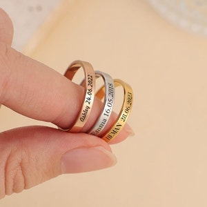 Peut inclure: Trois bagues fines en or, argent et or rose avec des dates et des noms gravés. Les bagues sont empilées les unes sur les autres.