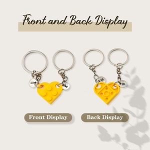 May include: Two yellow heart-shaped keychains with interlocking pieces, each with a silver ring and chain. The front of the keychain has a small silver charm with the letter 'K' on it. The back of the keychain has a small silver charm with the letter 'R' on it. The keychains are displayed on a white background with the text 'Front and Back Display' above them and 'Front Display' and 'Back Display' below them.