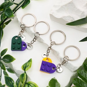 May include: Three silver keychains with heart-shaped charms made of Lego bricks. The charms are green and purple, purple and yellow, and green and purple. Each charm has a letter on the back: Z, N, and I.