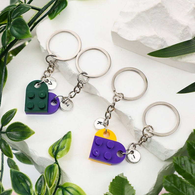 May include: Three silver keychains with heart-shaped charms made of Lego bricks. The charms are green and purple, purple and yellow, and green and purple. Each charm has a letter on the back: Z, N, and I.