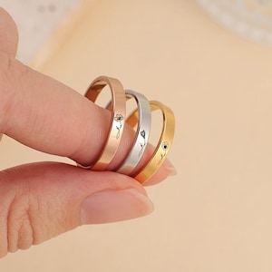 Op de afbeelding: Drie dunne ringen in roségoud, zilver en goud, elk gegraveerd met een delicaat bloemmotief. De ringen worden door een vinger omhoog gehouden, wat hun eenvoudige elegantie en potentieel om te stapelen laat zien. De ringen zijn een minimalistisch sieraad.