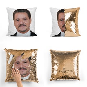 May include: A gold and white reversible sequin pillow with a picture of a man's face on one side. The pillow is 16 inches by 16 inches.
