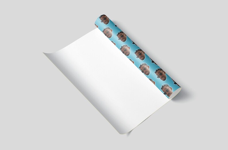 May include: A roll of wrapping paper with a repeating pattern of a person's face on a light blue background. The paper is partially unrolled, revealing a blank white surface. The image is set against a light gray background.