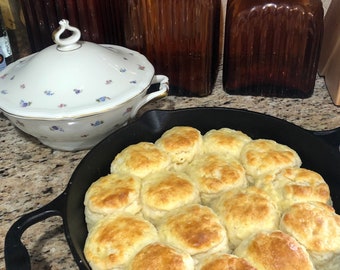 May include: A cast iron skillet filled with golden brown biscuits. The biscuits are arranged in a circle, with the edges slightly browned.