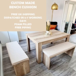 Puede incluir: Dos bancos de madera con cojines beige, una mesa de madera clara y una lámpara dorada en una habitación con suelo de madera clara. Los bancos y la mesa están en el centro de la imagen. El texto "CUSTOM MADE BENCH CUSHION" está en la parte superior de la imagen. El texto "FREE UK SHIPPING DISPATCHED IN 5-7 WORKING DAYS FOAM FILLED FREE PIPING" está debajo del texto "CUSTOM MADE BENCH CUSHION".