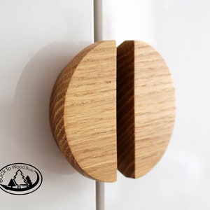 Könnte beinhalten: Zwei Holzknaufgriffe, die jeweils die Form eines Halbkreises haben, werden zu einem Kreis zusammengefügt. Die Griffe sind aus hellem braunem Holz mit natürlicher Maserung.
