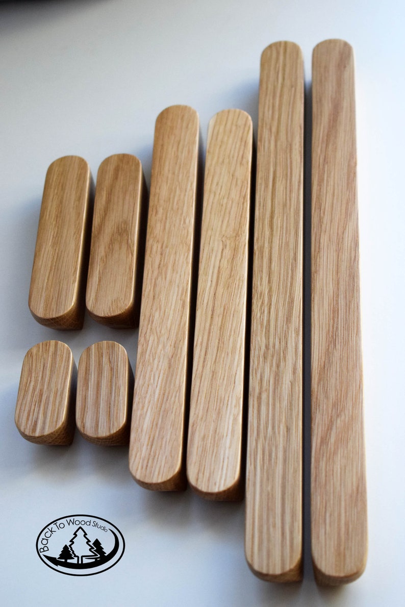 Pu&ograve; includere: Set di otto maniglie per cassetti in legno di diverse dimensioni. Le maniglie sono in legno marrone chiaro con finitura naturale. Le maniglie sono tutte di forma rettangolare con bordi arrotondati. Le maniglie sono disposte a scalare. Il testo "Back to Wood Studio" &egrave; visibile in un cerchio nella parte inferiore dell'immagine.