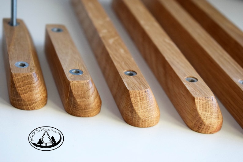 Pu&ograve; includere: Cinque maniglie per cassetti in legno con bordi arrotondati e finitura in legno naturale. Ogni maniglia &egrave; dotata di due viti argentate per l'installazione. Le maniglie sono disposte in fila su una superficie bianca.