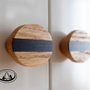 May include: Two round wooden cabinet knobs with a black stripe across the center. The knobs are made of light wood with a natural grain pattern.