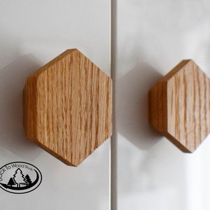 Op de afbeelding: Twee zeshoekige houten kastknoppen met een natuurlijke houtnerf afwerking. De knoppen zijn gemonteerd op een wit oppervlak. De tekst "Back to Wood Studio" is zichtbaar in de linkerbenedenhoek van de afbeelding.