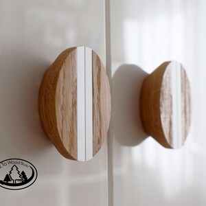 Könnte beinhalten: Zwei runde Holzknöpfe mit weißen vertikalen Streifen. Die Knöpfe sind auf einer weißen Oberfläche montiert.