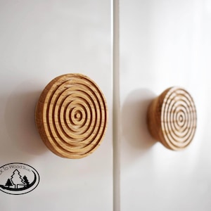 Può includere: Due pomelli per armadi in legno con un design a cerchi concentrici. I pomelli sono di colore marrone chiaro e hanno una finitura liscia.